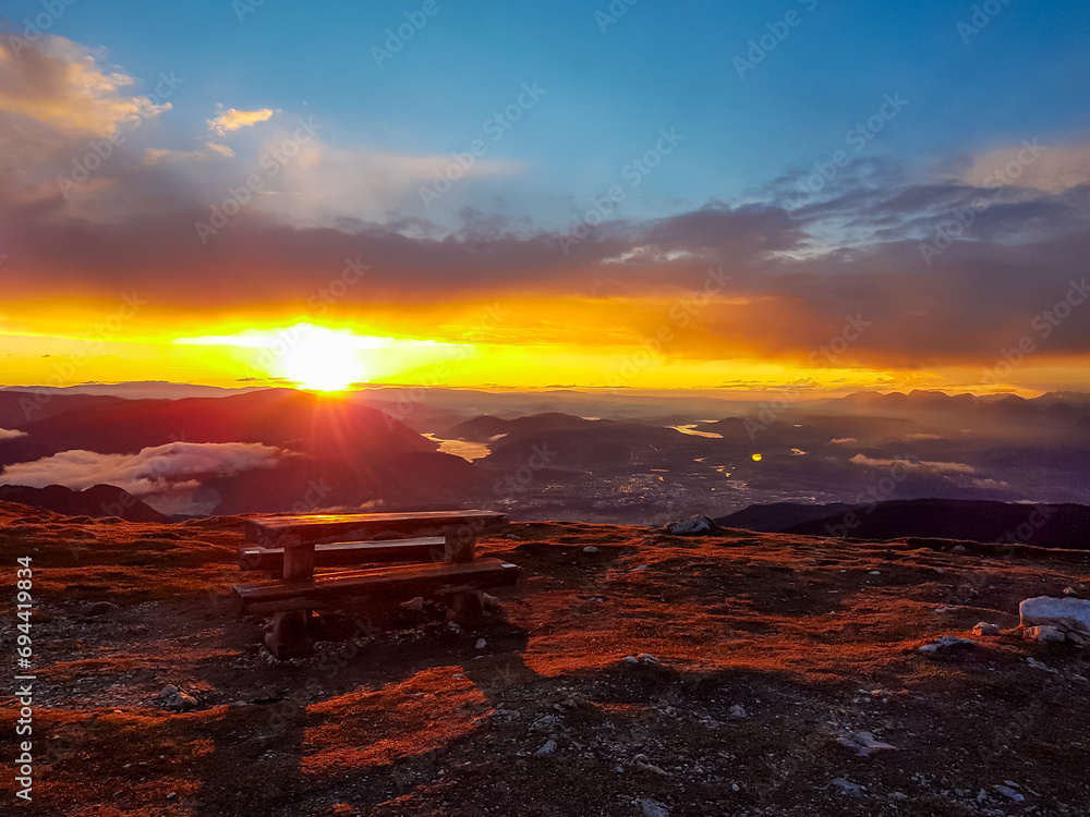 Panoramic sunrise view from summit Dobratsch on Julian Alps and Karawanks in Austria, Europe. Silhouette of endless mountain ranges with orange and pink colors of sky. Jagged sharp peaks and valleys