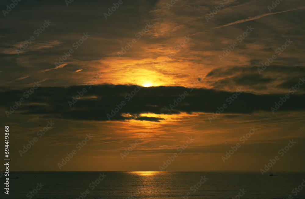 Fototapeta premium Entardecer deslumbrante, pintando o céu em tons dourados, onde nuvens suaves se entrelaçam. O mar, sereno e dourado, espelha os reflexos cintilantes dos raios solares, criando uma paisagem romântica.
