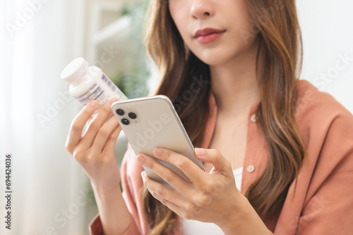 Health care asian young woman using smart phone for reading, searching prescription on bottle medicine, pill label text about information online, instructions side effects, pharmacy medicament concept photo