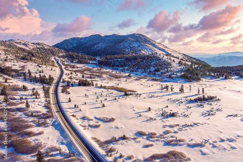Aerial view of  a Sunrise over Mt. Rose located near Reno and Lake Tahoe Nevada with magenta clouds, snow capped mountains and a winding road in the snow towards the background. photo