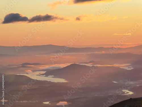 Panoramic sunrise view from Dobratsch on Julian Alps and Karawanks in Austria, Europe. Silhouette of endless mountain ranges. Lake Woerthersee (lake Woerth) surrounded by mysterious haze and fog