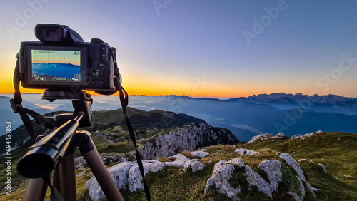 Professional camera setup at sunrise on mountain peak of Dobratsch, Villacher Alps, Carinthia, Austria, Europe. ilhouette of endless mountain ranges with orange and pink sky. Landscape photography