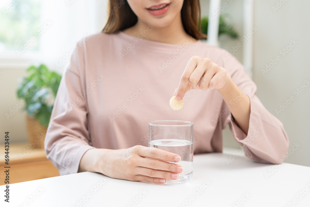 Smile asian young woman putting or dropping effervescent tablet into glass of water, holding pain pill, painkiller medicine, aspirin for treatment, take vitamin c for hangover. Health care concept. Smile asian young woman putting or dropping effervescent tablet into glass of water, holding pain pill, painkiller medicine, aspirin for treatment, take vitamin c for hangover. Health care concept.