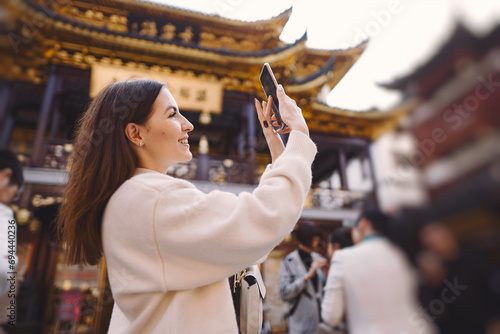 Photography brunette girl taking photos on her phone of a pagoda in Yuyuan