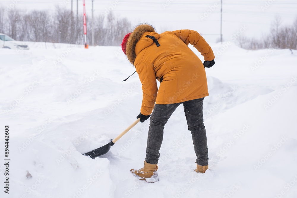 A man cleans and clears the snow in front of the house on frosty day. Cleaning the street from snow on a winter day. Snowfall and severe snowstorm in winter.