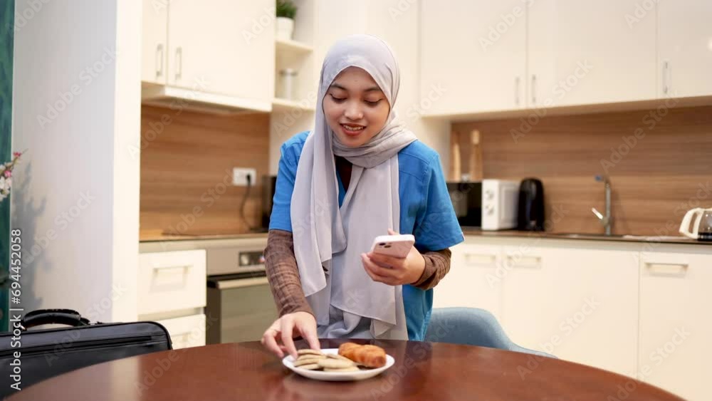 Young nurse having a breakfast and using smartphone at home, before heading to work Young nurse having a breakfast and using smartphone at home, before heading to work