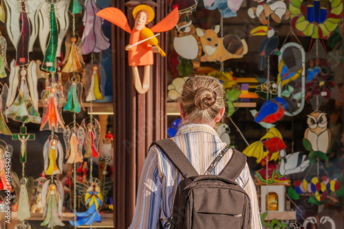 A woman admires bright, whimsical, colorful bells and decorations, including an orange fairy figure with wings holding a violin. Shopping, art and creativity concept