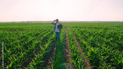 Agronomist on farm, Modern digital technologies. Farmer man in corn field works with computer, Business Farm. Agriculture Business concept. Farmer with laptop in green corn field. Businessman works
