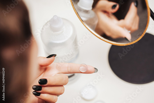 Contact lens background. Woman cleaning her contact lens. Lens liquid bottle. Girl hand with lens on finger.