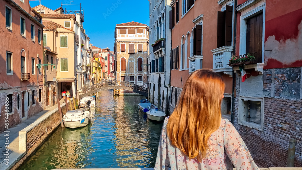 Rear view of woman watching water channel in city Venice, Veneto, Italy, Europe. Venetian architectural landmarks and old houses facades along. Urban tourism in summer atmosphere. Romantic vacation - obrazy, fototapety, plakaty 