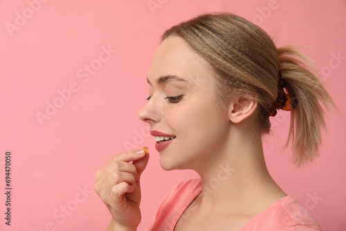 Young woman taking vitamin A pill on pink background, closeup