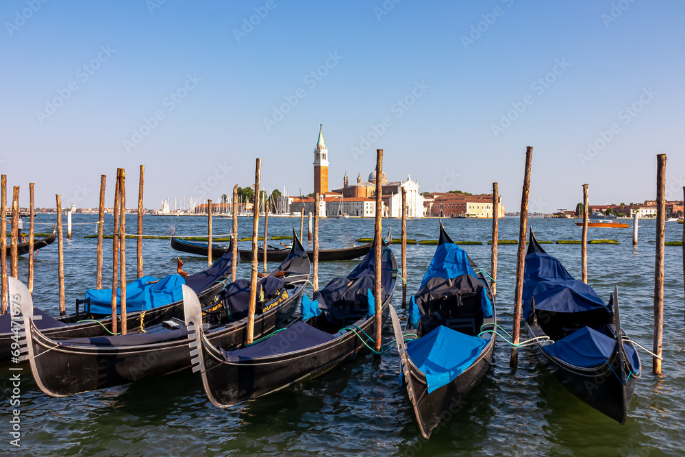 Group of gondolas moored by Saint Mark square in city of Venice, Veneto, Northern Italy, Europe. Scenic view of San Giorgio di Maggiore church in background. Romantic vacation in the Venetian Lagoon