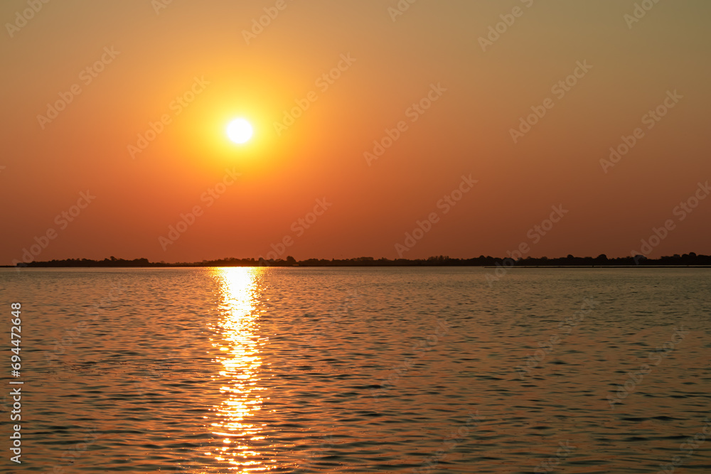 Scenic sunset view on San Michele island at Venetian lagoon in Venice, Veneto, Northern Italy, Europe. Reflection in the water creating romantic atmosphere. Orange red sky. Silhouette of landmarks
