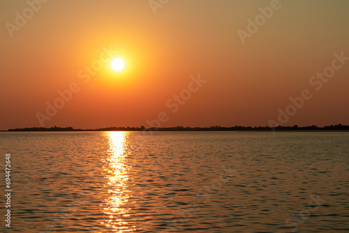 Scenic sunset view on San Michele island at Venetian lagoon in Venice, Veneto, Northern Italy, Europe. Reflection in the water creating romantic atmosphere. Orange red sky. Silhouette of landmarks © Chris