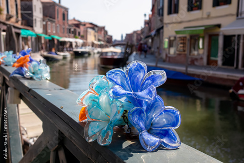 Murano glass flower with scenic view of clock tower and Ponte San Pietro Martire bridge over canal Rio dei Vetrai at Murano, island in the Venetian Lagoon near Venice, Veneto, Northern Italy, Europe