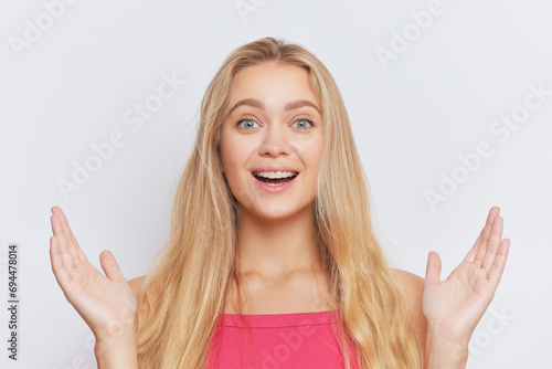 Close-up shot of blonde girl with long hair in pink top isolated on white background with hands up, good choice concept, copy space