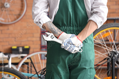 Fototapeta Naklejka Na Ścianę i Meble -  Young mechanic with wrench repairing bicycle in workshop, back view