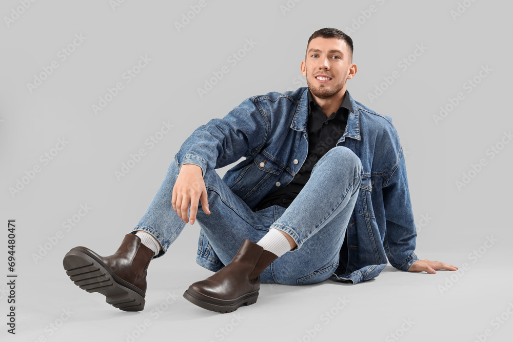 Stylish young man in denim clothes sitting on light background Stylish young man in denim clothes sitting on light background