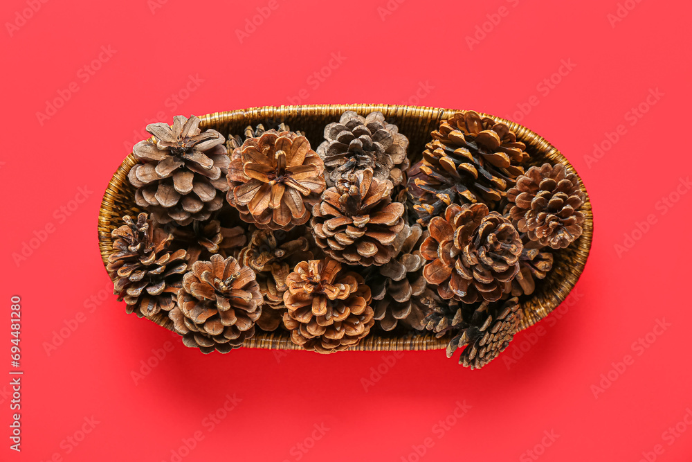 Wicker bowl with pine cones on red background Wicker bowl with pine cones on red background