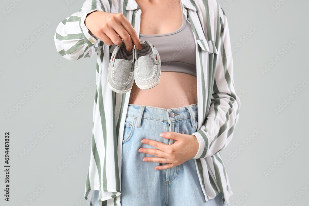 Young pregnant woman with baby booties on light background, closeup