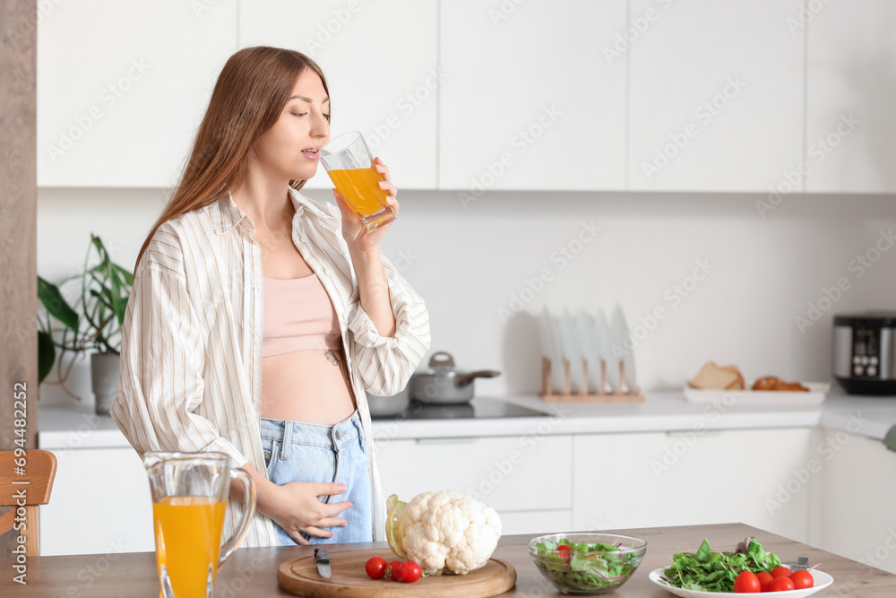 Young pregnant woman drinking juice in kitchen