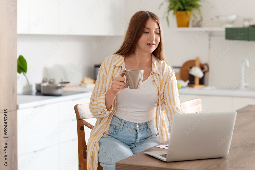 Young pregnant woman with cup of tea using laptop in kitchen Young pregnant woman with cup of tea using laptop in kitchen