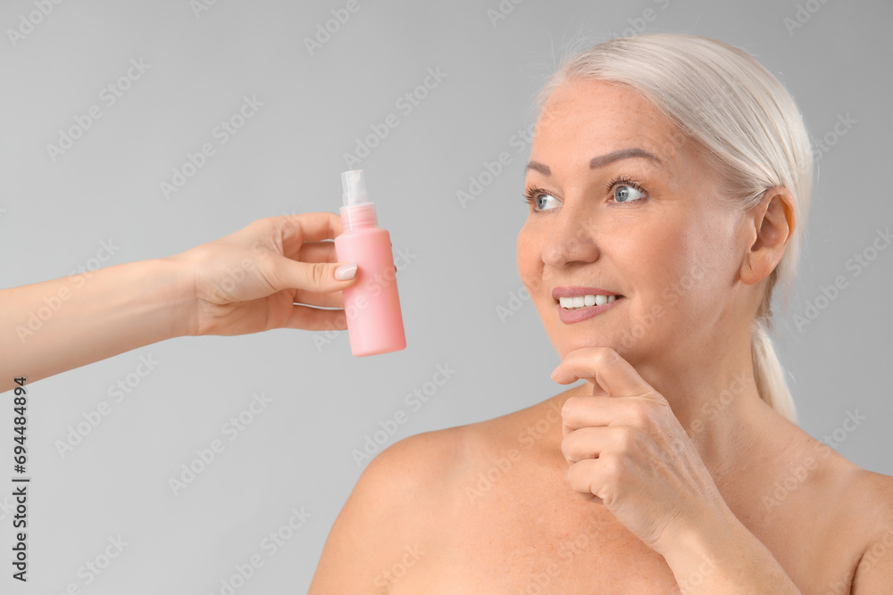 Φωτογραφία Beautiful mature woman and hand with bottle of skincare product on light backgro