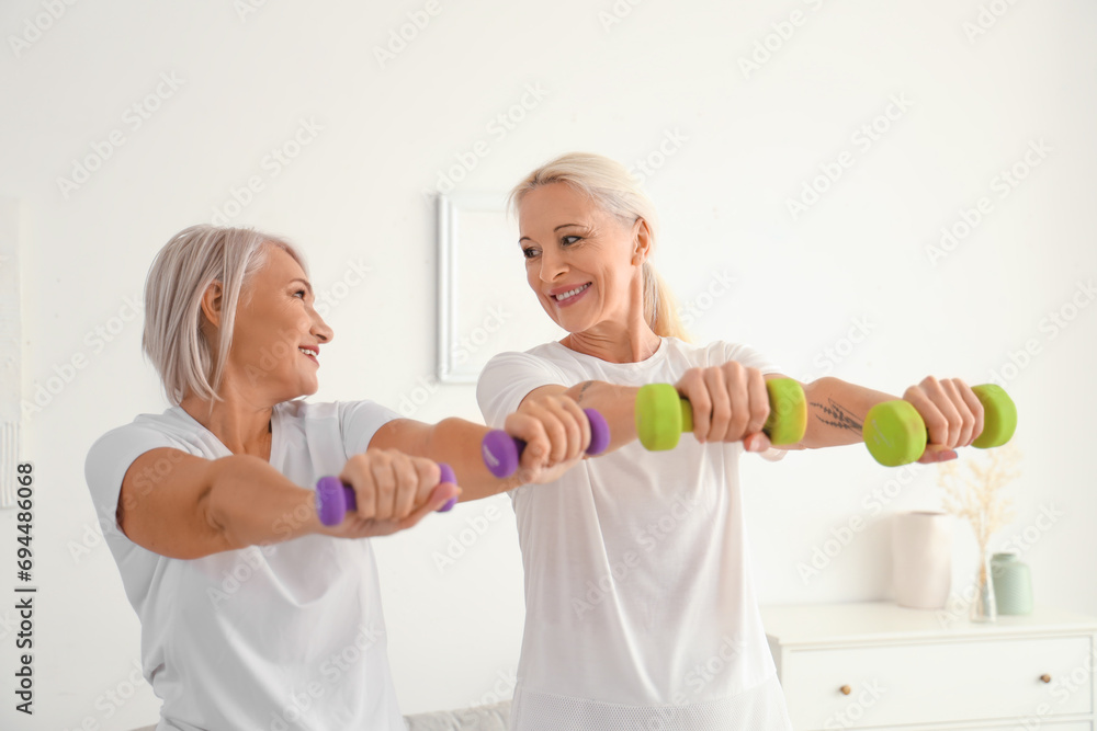 Mature female friends with dumbbells training at home