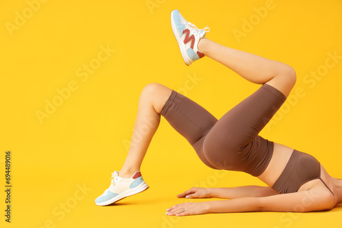Young woman in cycling shorts lying on yellow background photo