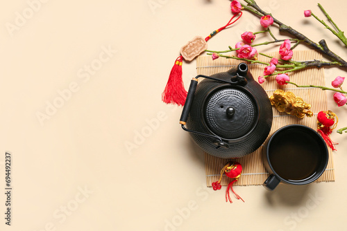 Golden dragon figure with teapot, cup of tea and branch of flowers on beige background. Chinese New Year celebration