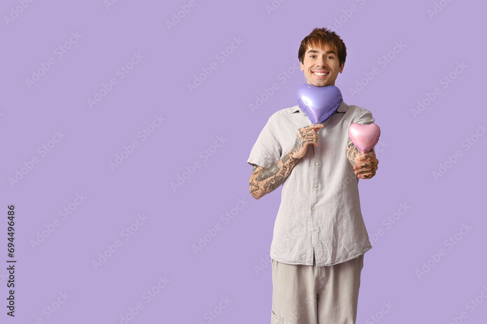 Handsome young man with air balloons in shape of heart on lilac background. Valentine's Day celebration Handsome young man with air balloons in shape of heart on lilac background. Valentine's Day celebration