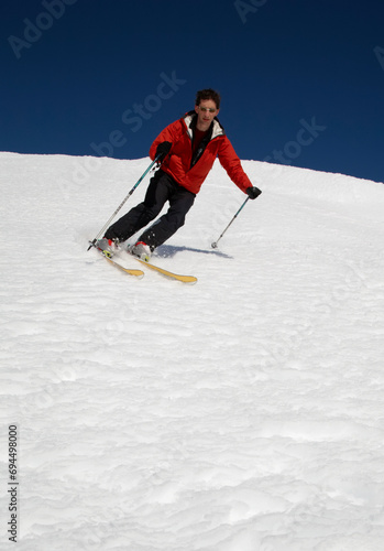 This image captures the thrilling sport of skiing, set against a backdrop of a pristine, snowy hill. The central figure is a man, fully equipped with skiing gear and engaged in a exhilarating downhill
