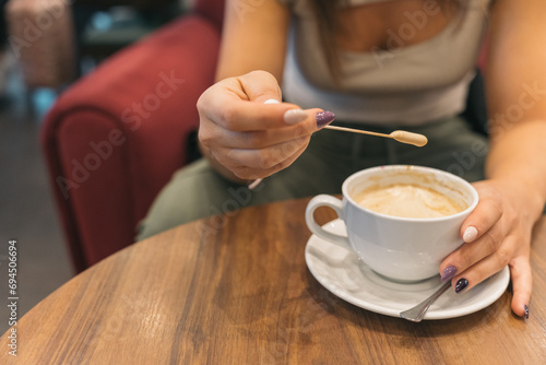 Unrecognizable woman tasting the froth of her sweet coffee. Close up image of an anonymous young girl taking freshly brewed foam out of her coffee to taste it.