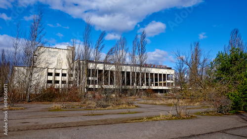 A dilapidated building with broken windows  surrounded by overgrown vegetation and bare trees. The Energetik Palace of Culture is a now abandoned multifunctional palace of culture in Pripyat.