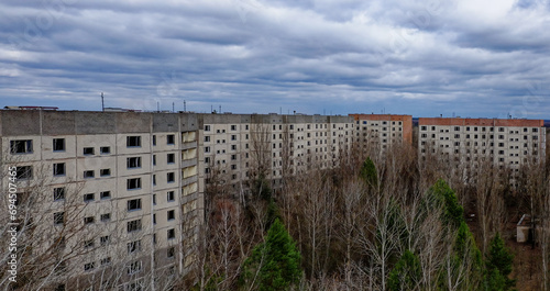 A cloudy sky above a series of old, grey apartment buildings surrounded by bare trees.