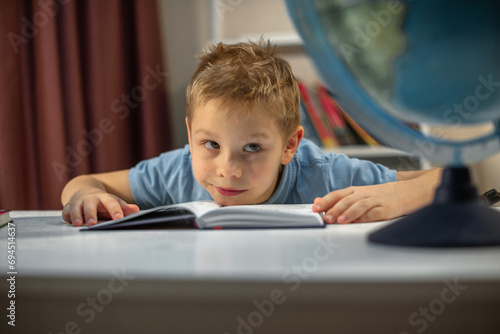 blond boy doing homework at home, tired and looking at the globe on the table
