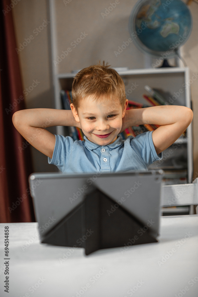 A blond boy sits in his room at his tablet. smiles and watches the video with pleasure A blond boy sits in his room at his tablet. smiles and watches the video with pleasure