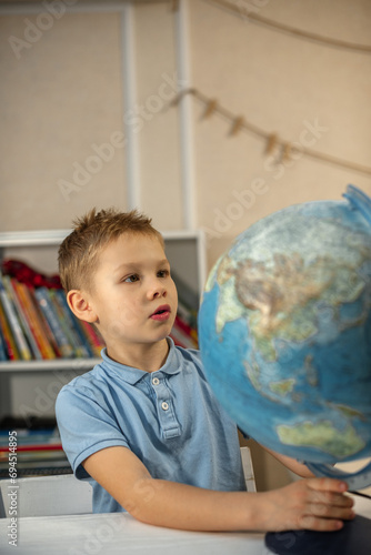 A cute caicasian blond boy in a blue T-shirt looks at the globe with interest. searches for the country in which he lives photo