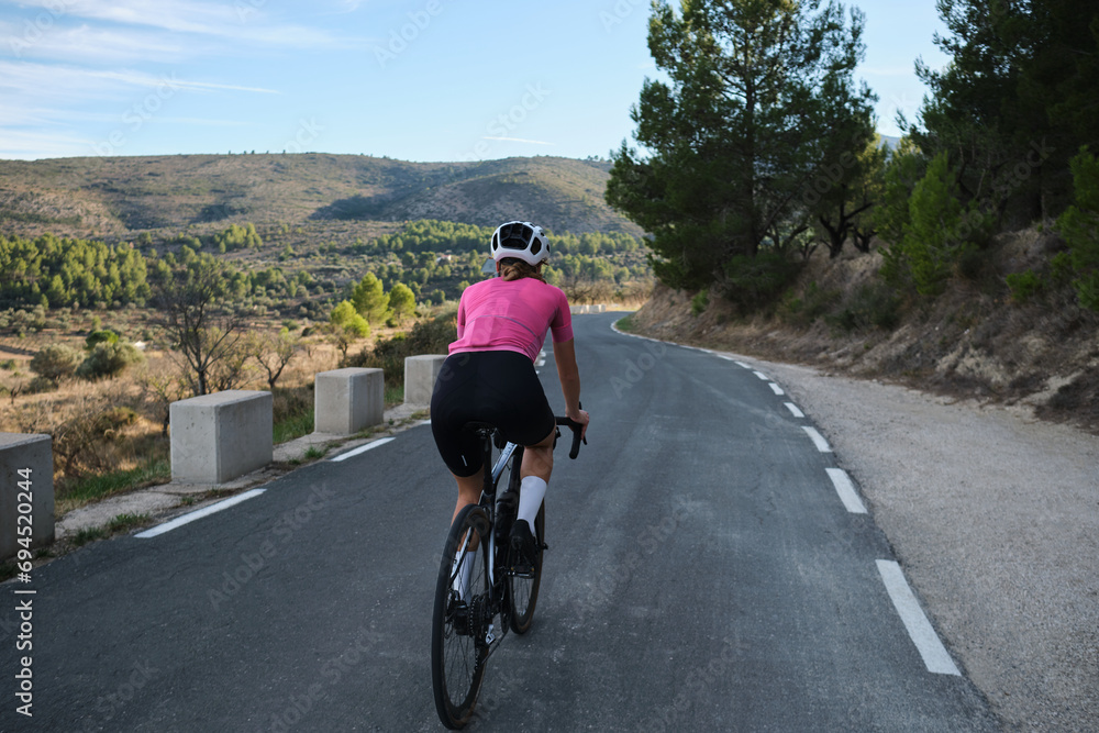 Fit female cyclist riding a gravel bike with a view of the Spanish mountains. Athlete wearing sportswear and helmet. Sports motivation image. Good road for cycling. Mountain Bernia, Alicante, Spain.