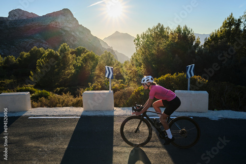 Woman cyclist wearing cycling kit and helmet riding on the road on a gravel bike at sunset.Empty mountain road. Sports motivation image. Bernia mountain in Spain. photo