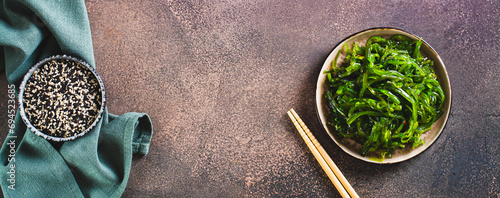 Delicious wakame seaweed salad on a plate and sesame seeds in a bowl top view web banner