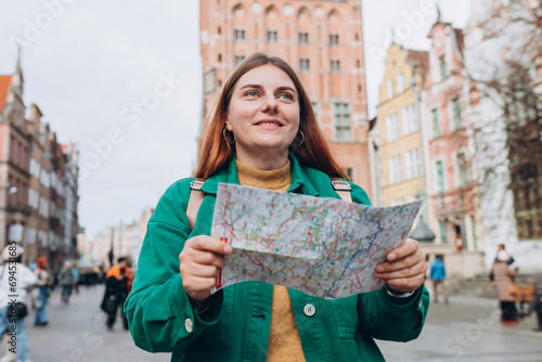 Portrait beautiful woman with paper map in street. Happy tourist travels in Europe. Vacation concept by exploring interesting places to travel. Women Searching locations at autumn day. Gdansk, Poland