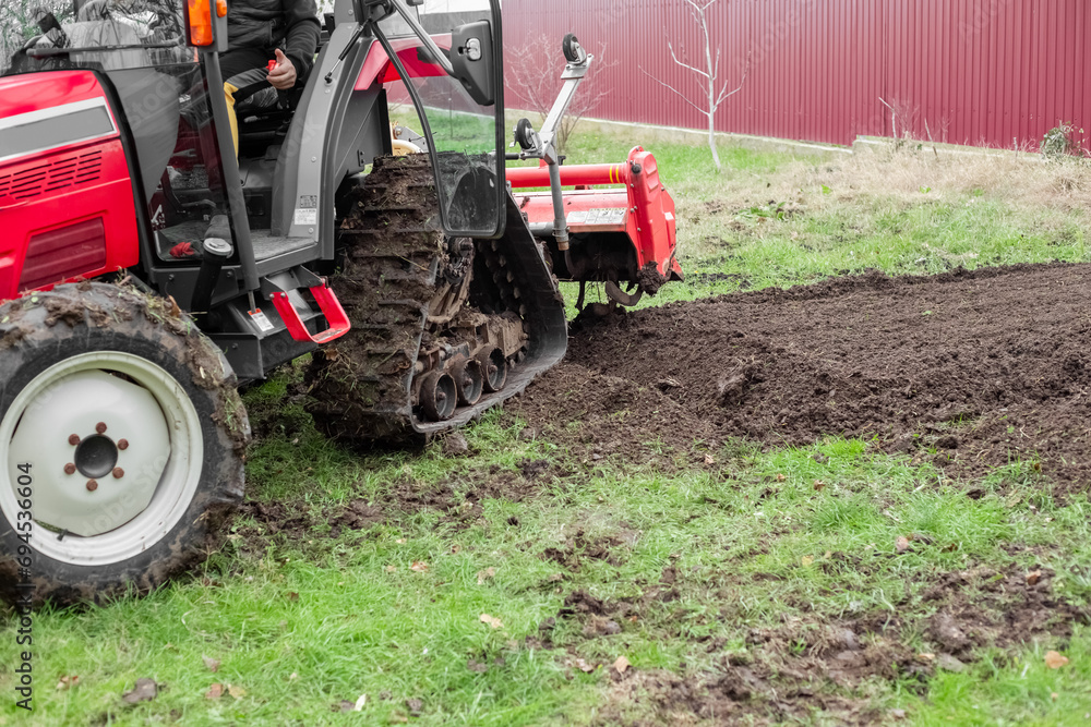 A mini tractor with a milling machine plows the ground on an agricultural field on an autumn day. A mini tractor with a milling machine plows the ground on an agricultural field on an autumn day.