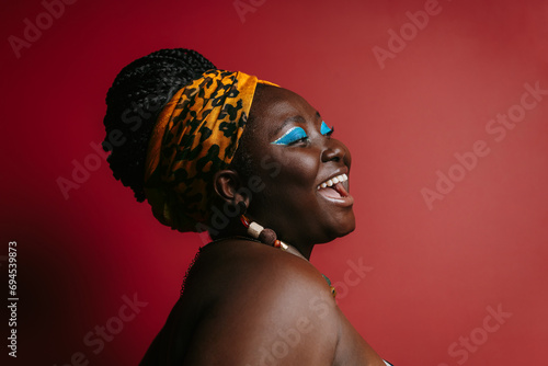 Happy plus size African woman with colorful make-up wearing traditional headwear on red background
