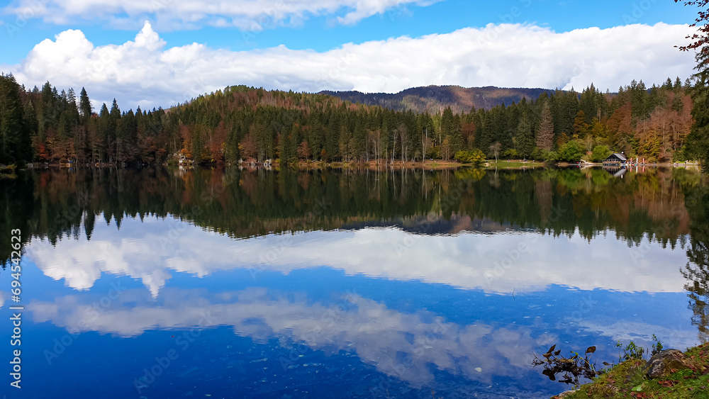 Panoramic view of Fusine Lake (Laghi di Fusine) in Tarvisio, Friuli-Venezia Giulia, Italy, Europe. Water reflection in clear green alpine lake. Autumn colored foliage. Calm serene tranquil atmosphere