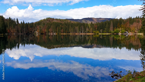 Panoramic view of Fusine Lake (Laghi di Fusine) in Tarvisio, Friuli-Venezia Giulia, Italy, Europe. Water reflection in clear green alpine lake. Autumn colored foliage. Calm serene tranquil atmosphere