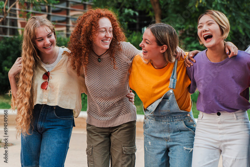 Group of joyful college student women in casual clothing, laughing and enjoying a nice weekend. Real cool girls walking embracing with toothy smile together. Happy female friends having fun outside