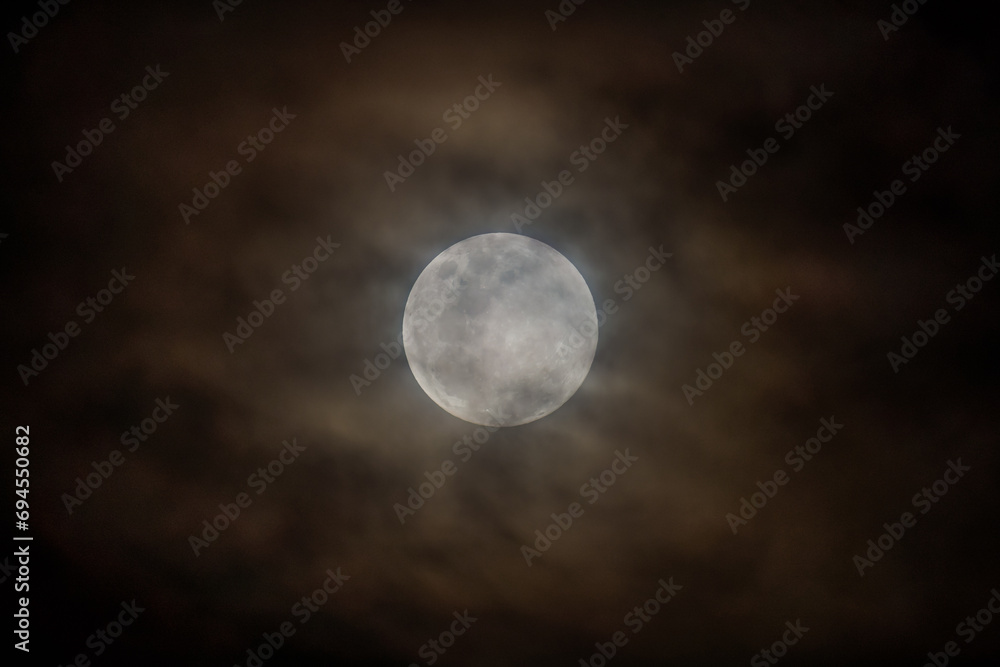 Earth's moon rising at 99 percent full with high cloud in the night sky Earth's moon rising at 99 percent full with high cloud in the night sky