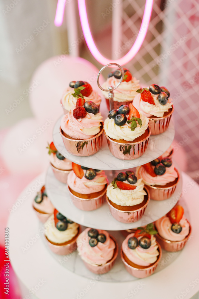 A plate of cupcakes decorated with white and pink cream with berries. 