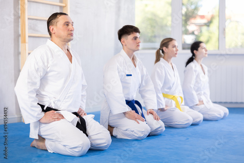 Group of men and women karatekas in kimonos posing while sitting on floor in studio..